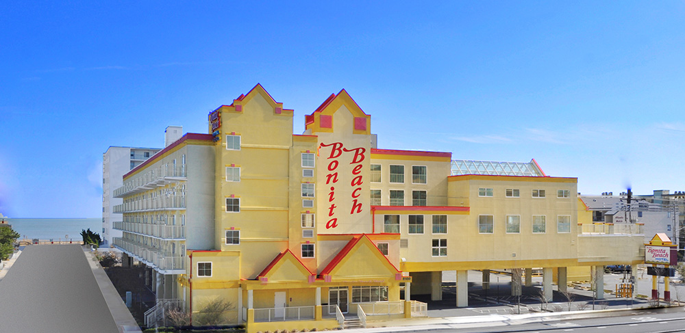 a large yellow hotel with a red roof next to the ocean